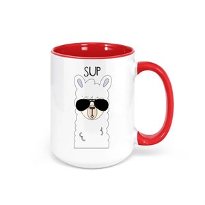 May include: White ceramic mug with a red interior and handle. The mug features a cartoon llama wearing sunglasses, with the word "SUP" above the llama's head. The mug is designed for beverages.