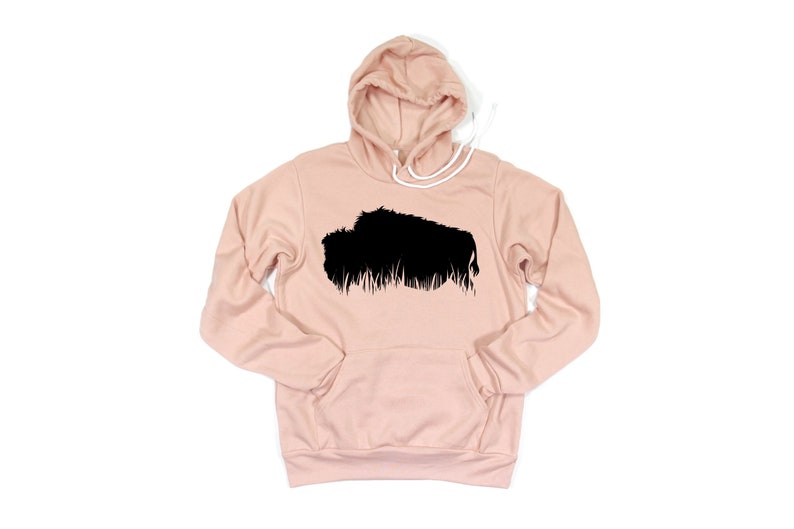 May include: A light pink hoodie with a black graphic of a bison. The hoodie has a drawstring hood and a front pocket. The bison graphic is a silhouette with a textured, grassy base.