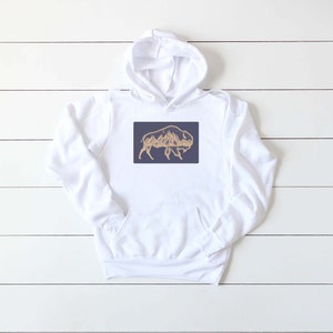 May include: White hooded sweatshirt with a navy blue rectangle featuring a gold outline of a bison with mountains inside the silhouette.