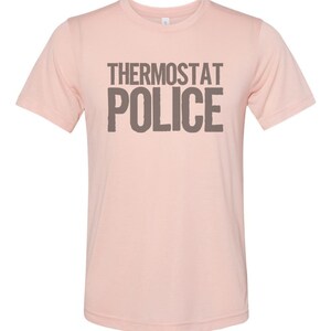 May include: A pink t-shirt with the text "Thermostat Police" printed in brown on the front.