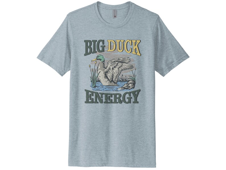 May include: A light blue t-shirt with a vintage-style graphic of a duck in a pond. The text "BIG DUCK ENERGY" is printed in yellow and green letters.