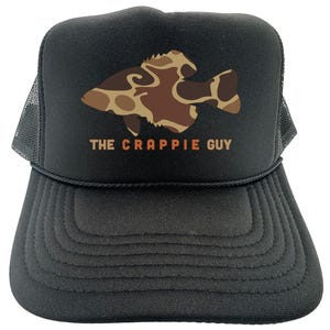May include: Black trucker hat with a brown and tan camouflage fish graphic and the text "The Crappie Guy" in orange.