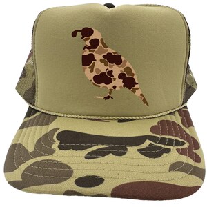 May include: A camouflage trucker hat with a brown and tan camouflage pattern. The front of the hat features a brown and tan camouflage quail silhouette.