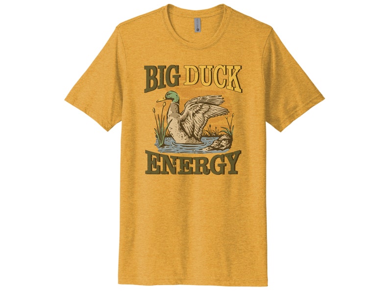 May include: A yellow t-shirt with a vintage-style illustration of a duck on a pond. The text "BIG DUCK ENERGY" is printed in brown letters on the shirt.