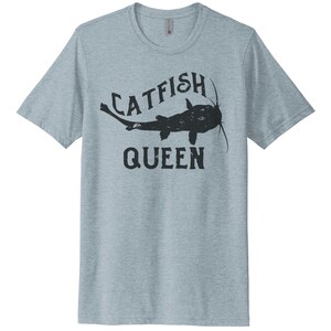 May include: A light blue t-shirt with a black catfish graphic and the text "Catfish Queen".