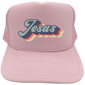 Puede incluir: Gorra de camionero rosa con un gr&aacute;fico retro de "Jes&uacute;s" en colores arco&iacute;ris.