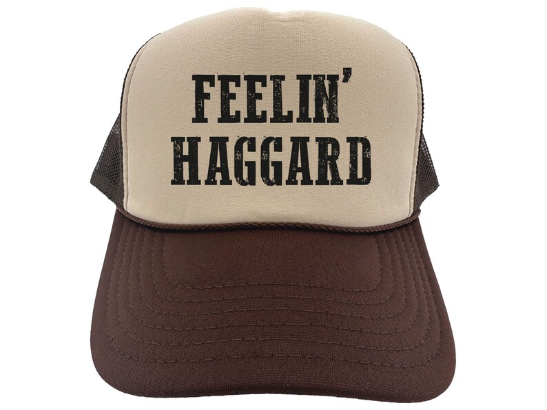 May include: A brown and beige trucker hat with a black mesh back. The front of the hat has the text "FEELIN' HAGGARD" printed in black.