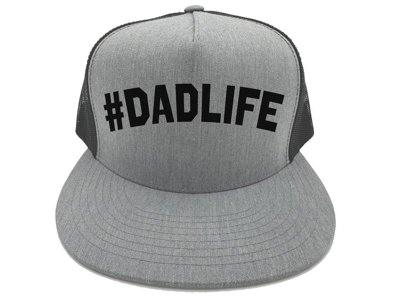 May include: A gray trucker hat with a black mesh back and a flat brim. The hat features the text "#DADLIFE" in bold, black letters across the front.