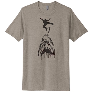 May include: A heather grey t-shirt with a black graphic of a shark's mouth with a silhouette of a person skateboarding over it.