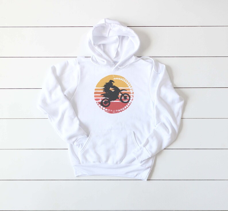 May include: White hooded sweatshirt with a graphic of a person riding a dirt bike in front of a sunset. The graphic is in a circle with a tire tread pattern around the edge.