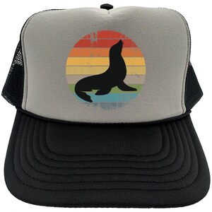 May include: A gray and black trucker hat with a vintage-style graphic of a seal silhouette in front of a rainbow sunset.