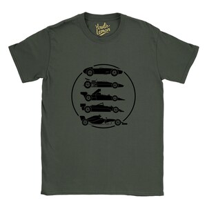 Op de afbeelding: Donkergroen t-shirt met een zwarte afbeelding van vijf raceauto's in een zwarte cirkel. Het shirt heeft de tekst "Howlin' Lemon" in het geel. De auto's zijn in silhouet, die verschillende tijdperken van de race vertegenwoordigen.