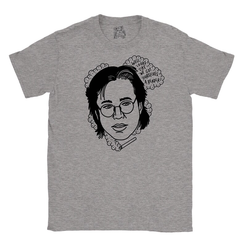 May include: A grey t-shirt featuring a black and white illustration of a person wearing glasses and holding a cigarette. The text "Well, looks like we got ourselves a reader?" is in a speech bubble above the person's head.