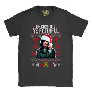May include: A black t-shirt featuring a Christmas-themed design. The design includes the text "OH COME ALL YE FAITHFUL" above a portrait of a person wearing a Santa hat. Red ribbons, snowflakes, and reindeer complete the festive look.