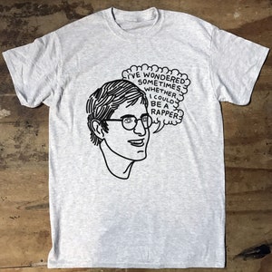 May include: Pale grey t-shirt with a black line drawing of a person wearing glasses and a thought bubble. The thought bubble says: "I'VE WONDERED SOMETIMES, WHETHER I COULD BE A RAPPER."