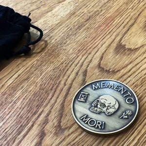 May include: A gold-toned metal coin with the words "Memento Mori" and an hourglass, skull, and rose design.