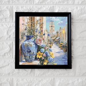 May include: A framed painting of a European street scene, featuring a blue vase filled with flowers. The painting shows a blue and white vase, pink roses, yellow and blue flowers, and a distant church with a blue dome.