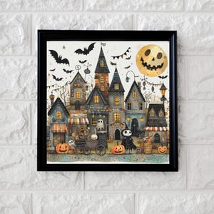 May include: A framed Halloween-themed print featuring a whimsical village scene. The artwork showcases a smiling moon, bats, and a variety of spooky houses with jack-o'-lanterns. The print is set against a white brick background.