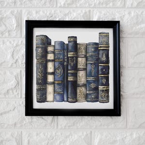 May include: A framed print featuring a collection of antique books. The books have navy blue covers with gold accents and ornate designs. The print is in a black frame and is displayed against a white brick wall.