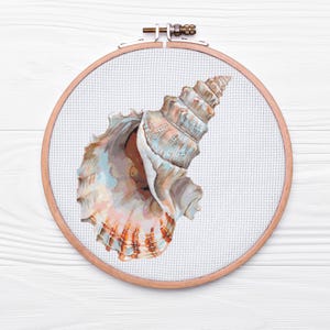 Puede incluir: Un primer plano de un proyecto de bordado de punto de cruz con una concha marina en un aro de bordado de madera. La concha es de color azul claro y marrón y tiene una forma espiral.