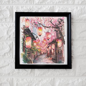 Puede incluir: Una impresión enmarcada que representa una escena callejera japonesa. La obra de arte muestra un camino bordeado de edificios tradicionales y faroles de papel. Los cerezos en flor con flores rosas arquean sobre la calle, creando una vista pintoresca.
