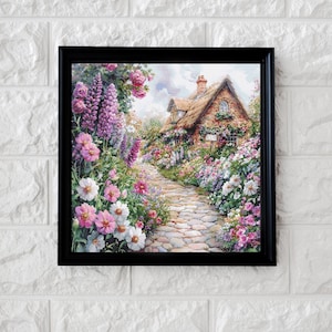 May include: Framed print of a cottage scene. The artwork depicts a stone path leading to a thatched-roof cottage, surrounded by a vibrant garden of pink, purple, and white flowers. The print is encased in a black frame.