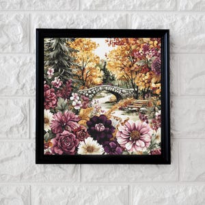 Könnte beinhalten: Gerahmtes Aquarellgemälde einer Steinbrücke über einem Bach, umgeben von farbenfrohem Herbstlaub und Blumen. Das Kunstwerk hat einen schwarzen Rahmen und einen weißen Ziegelhintergrund. Die Blumen sind in Rosa-, Lila- und Weißtönen gehalten.