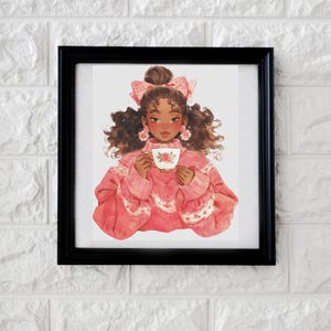 Op de afbeelding: Een ingelijste kunstdruk met een jonge persoon met krullend haar, gekleed in een roze trui en een kopje thee vasthoudend. De illustratie heeft een zachte aquarel stijl met roze en witte bloemaccenten. De lijst is zwart.