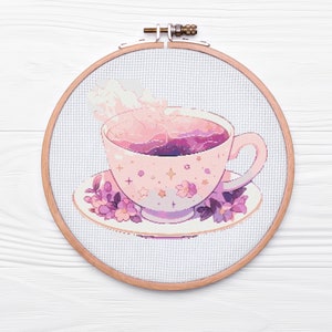 Puede incluir: Una taza de té rosa con un diseño de remolino morado y rosa en el interior, con vapor que sale de la parte superior. La taza de té está sobre un platillo con flores moradas y estrellas.