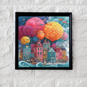 Könnte beinhalten: Ein gerahmter Wandkunstdruck, der eine bunte Stadt mit mehrstöckigen Gebäuden in Blau-, Rosa- und Gelbtönen an einem welligen blauen Meer zeigt. Über der Stadt schweben große, texturierte, kugelförmige Wolken in Rosa und Gelb am Himmel.