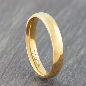 May include: A gold titanium wedding band with a polished finish. The band is inscribed with the word "TITANIUM".