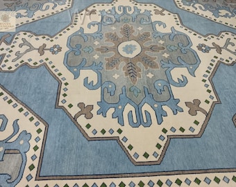 Puede incluir: Una alfombra grande, de color azul claro y crema, con un intrincado diseño geométrico. La alfombra presenta un diseño de medallón central con motivos florales y estilizados en tonos azules, grises y marrones. El borde es azul oscuro con detalles verdes y marrones.