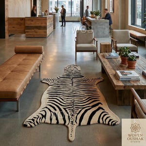Puede incluir: Una alfombra con estampado de cebra en crema y negro en un interior moderno. El patrón de la alfombra imita el pelaje de una cebra. La alfombra está colocada sobre un suelo de hormigón, con un banco de cuero y muebles de madera en el fondo.
