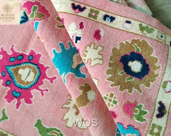 May include: A rolled-up pink rug with intricate floral and geometric patterns in shades of blue, green, brown, and white. The rug has a soft, textured appearance and features the text "WOS".
