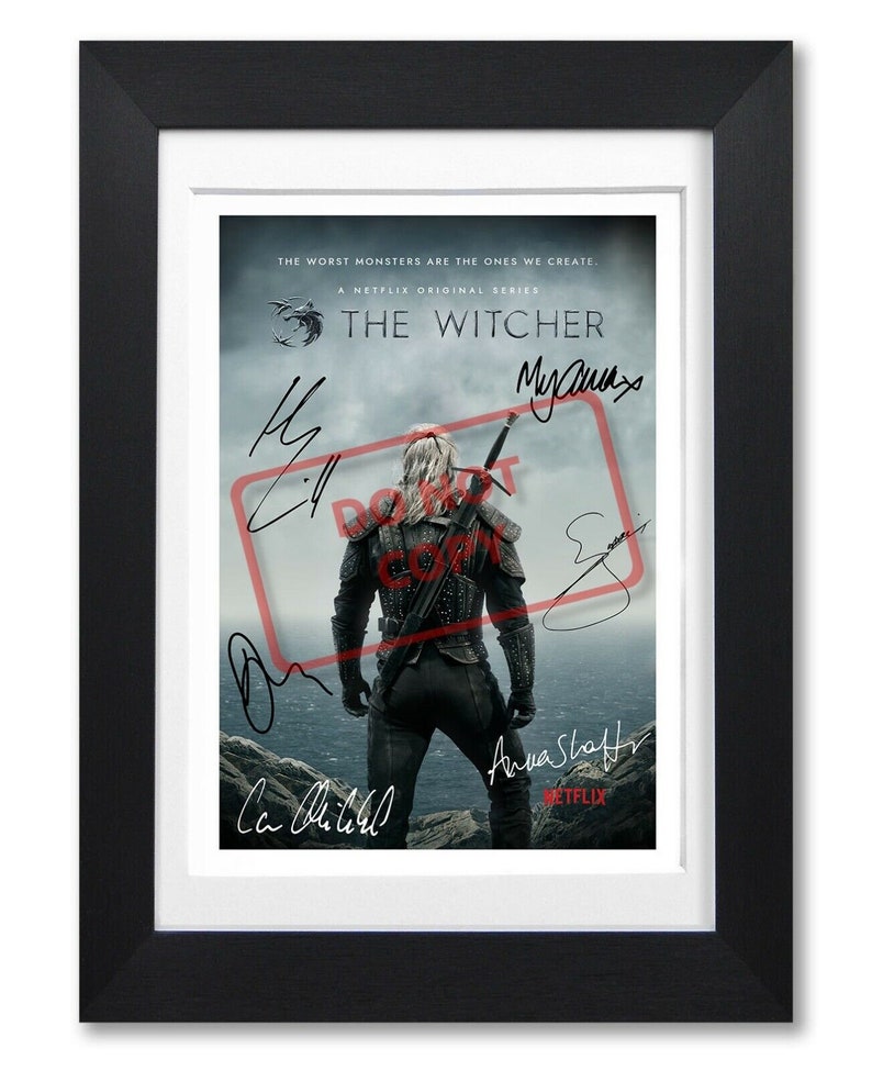 May include: A black and white poster for the Netflix series "The Witcher" featuring a man in a dark leather jacket and pants standing on a cliff overlooking a stormy sea. The poster has the text "The Witcher" and "The worst monsters are the ones we create." The poster is signed by the actors who play Geralt, Yennefer, and Ciri.