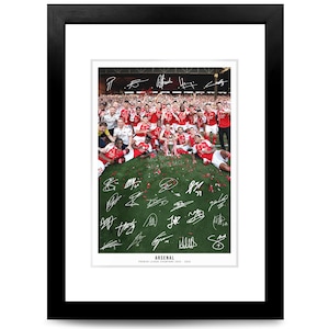 May include: A framed photograph of the Arsenal football team celebrating on a green pitch, featuring numerous white ink signatures overlaid on the image. The text at the bottom reads ARSENAL PREMIER LEAGUE CHAMPIONS 2023 - 2024.