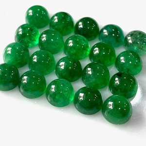 May include: A collection of twenty green emerald cabochons, each with a smooth, rounded surface. The cabochons are arranged in a loose, overlapping pattern.