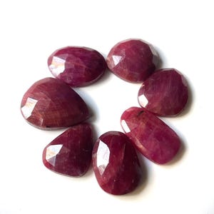 Pu&ograve; includere: Sette pietre preziose di rubino sfaccettate in una variet&agrave; di dimensioni e forme. Le pietre preziose sono di colore rosso intenso e hanno una finitura lucida.