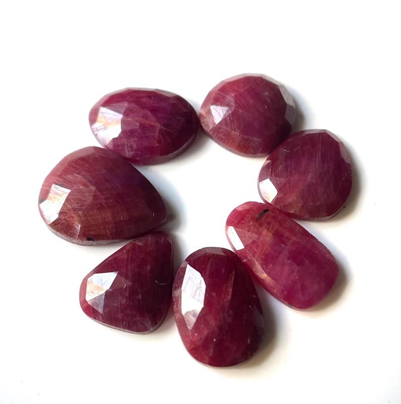 Pu&ograve; includere: Sette pietre preziose di rubino sfaccettate in una variet&agrave; di dimensioni e forme. Le pietre preziose sono di colore rosso intenso e hanno una finitura lucida.