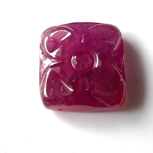 Op de afbeelding: Een gesneden robijn edelsteen met een bloemmotief. De edelsteen is dieprood en heeft een glanzende afwerking.