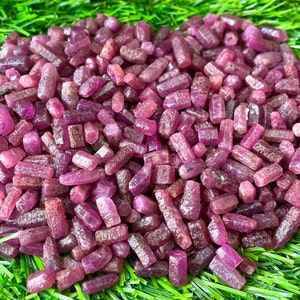 May include: A large pile of small, rough, pink ruby crystals. The crystals are all different sizes and shapes, but they are all a deep pink color.