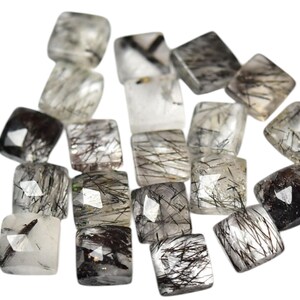 May include: A collection of 16 faceted, square-shaped, clear quartz crystals with black inclusions. The crystals are arranged in a random pattern on a white background.
