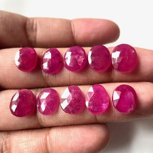 Puede incluir: Nueve piedras preciosas de rubí facetadas de diferentes tamaños y formas, mostradas en una mano.