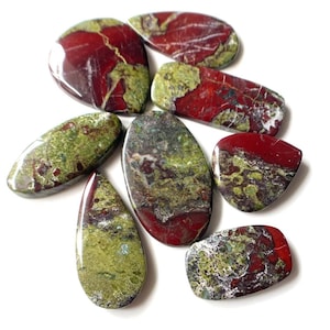 以下が含まれることがあります： 緑と赤のジャスパーの、涙滴型の研磨されたカボションが9つ集まったものです。石は、緑、赤、白の渦巻き模様が入り、まだらで、大理石のような外観をしています。