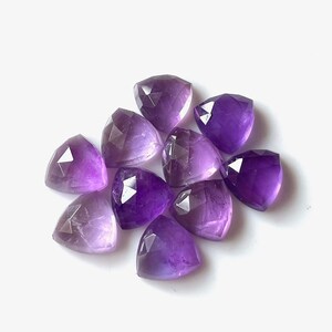 Könnte beinhalten: Eine Gruppe von zehn facettierten Amethyst-Edelsteinen in dreieckiger Form. Die Steine sind in verschiedenen Violetttönen, von hell bis dunkel.