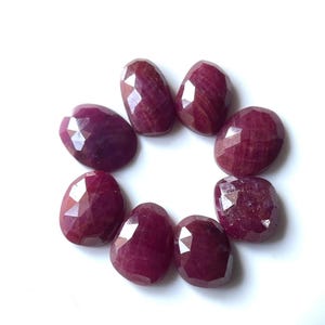 Può includere: Otto pietre preziose di rubino sfaccettate di colore rosso, disposte in cerchio su uno sfondo bianco.