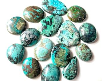 Op de afbeelding: Een verzameling van 14 turquoise cabochons in verschillende tinten blauw en groen met bruine en zwarte markeringen. De cabochons zijn ovaal en druppelvormig.