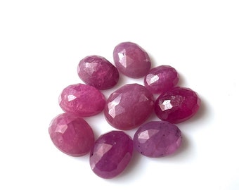 May include: A group of ten faceted oval-shaped pink gemstones. The gemstones are arranged in a loose cluster on a white background.