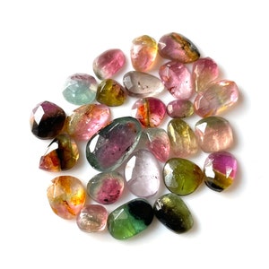 May include: A collection of 20 faceted, multi-colored gemstones. The stones are various shades of pink, green, yellow, and black. The stones are all cut in a similar shape, with a rounded top and a flat bottom.