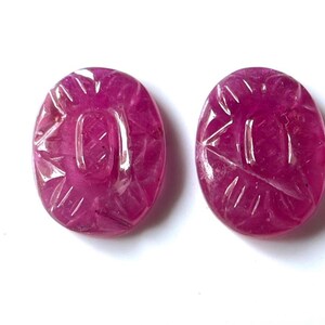 Puede incluir: Dos piedras preciosas de rubí talladas de forma ovalada, de color rosa intenso. Las piedras preciosas tienen un diseño tallado en la superficie.